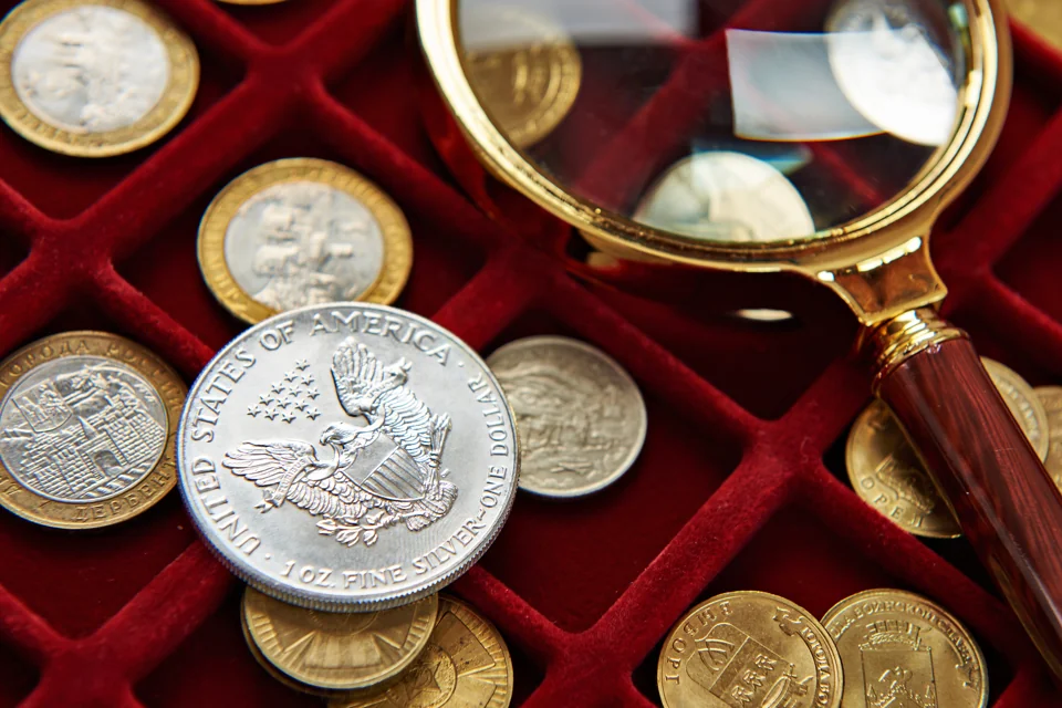 A collector's tray of coins with a magnifying glass, one American Silver Eagle in focus