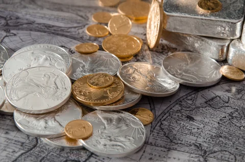 Gold and silver coins beside cast silver bars