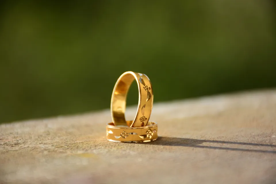 Two engraved gold bands, one standing inside the other, on a sunlit stone ledge